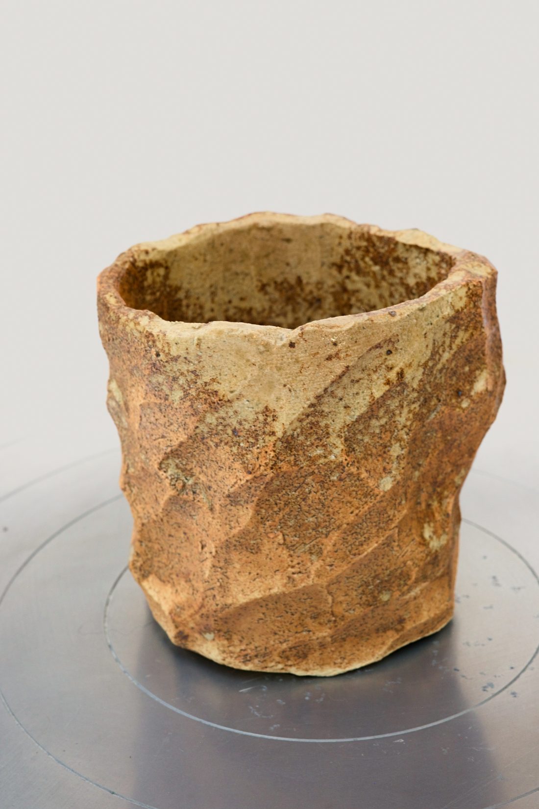 Raw Cup — faceted tumbler in unglazed clay with a torn rim.